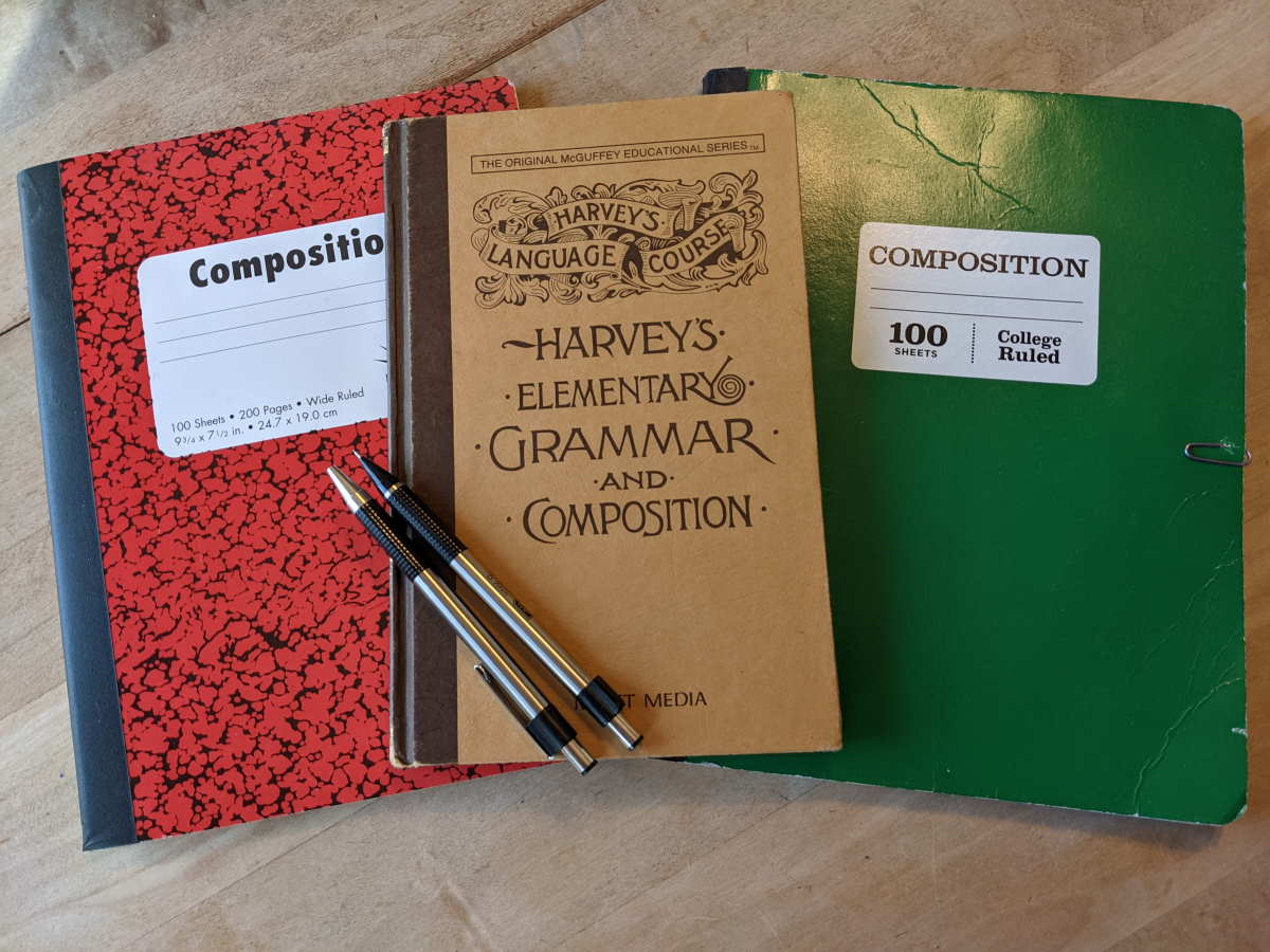 Harvey Grammar book with red and green composition notebooks and a mechanical pen and pencil.